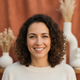 Portrait of a smiling woman, mid-30s, with a look of satisfaction against a warm, soft-focus background.